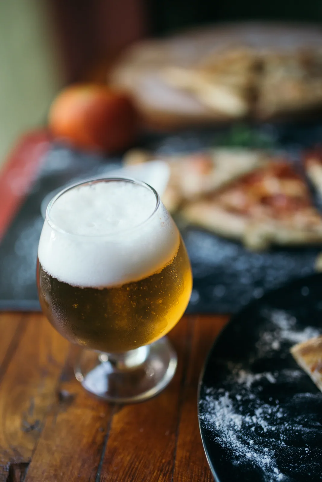 A glass of craft beer with pizza on a nearby plate.