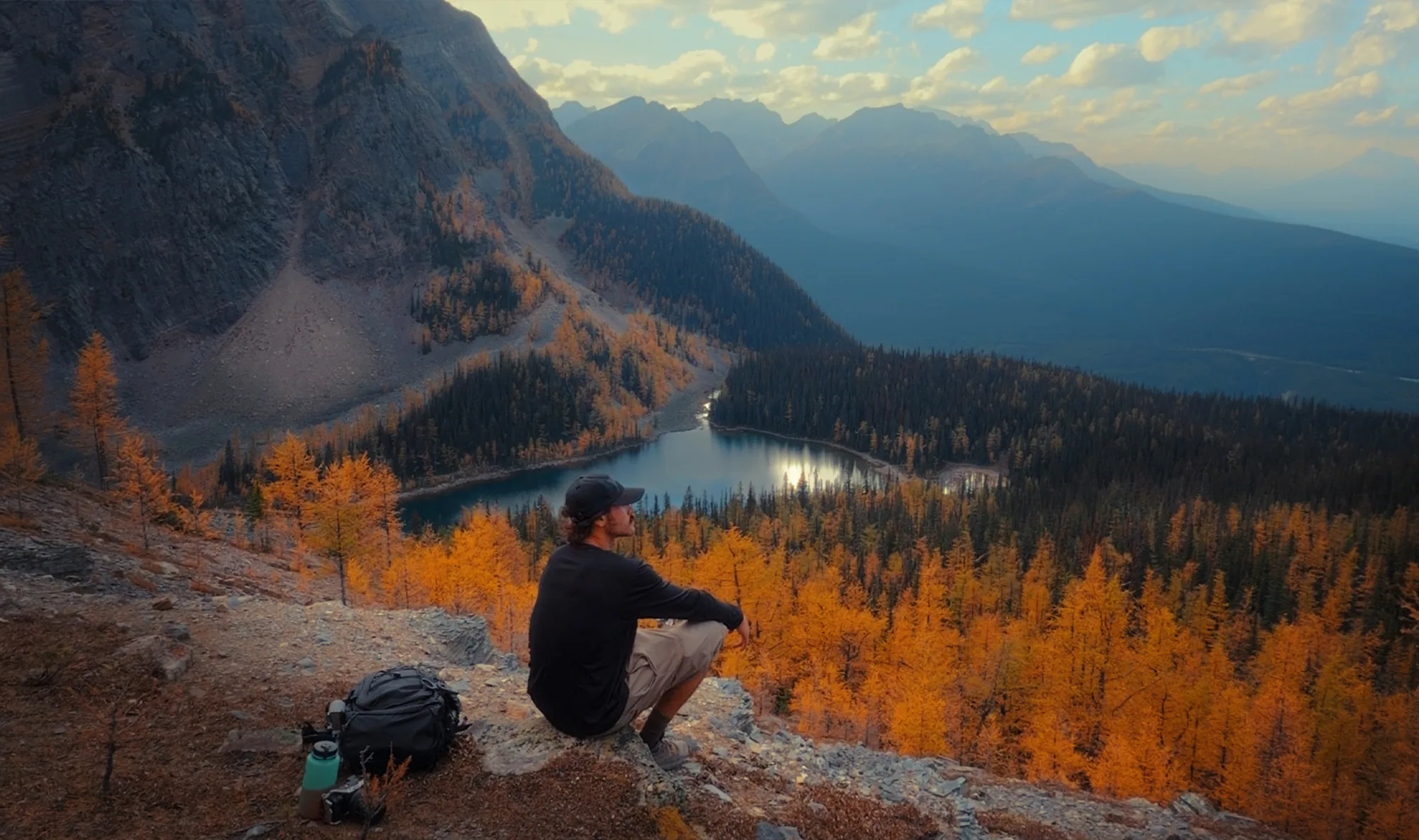 A hiker overlooking Twin Lakes and a mountainside of golden larches.