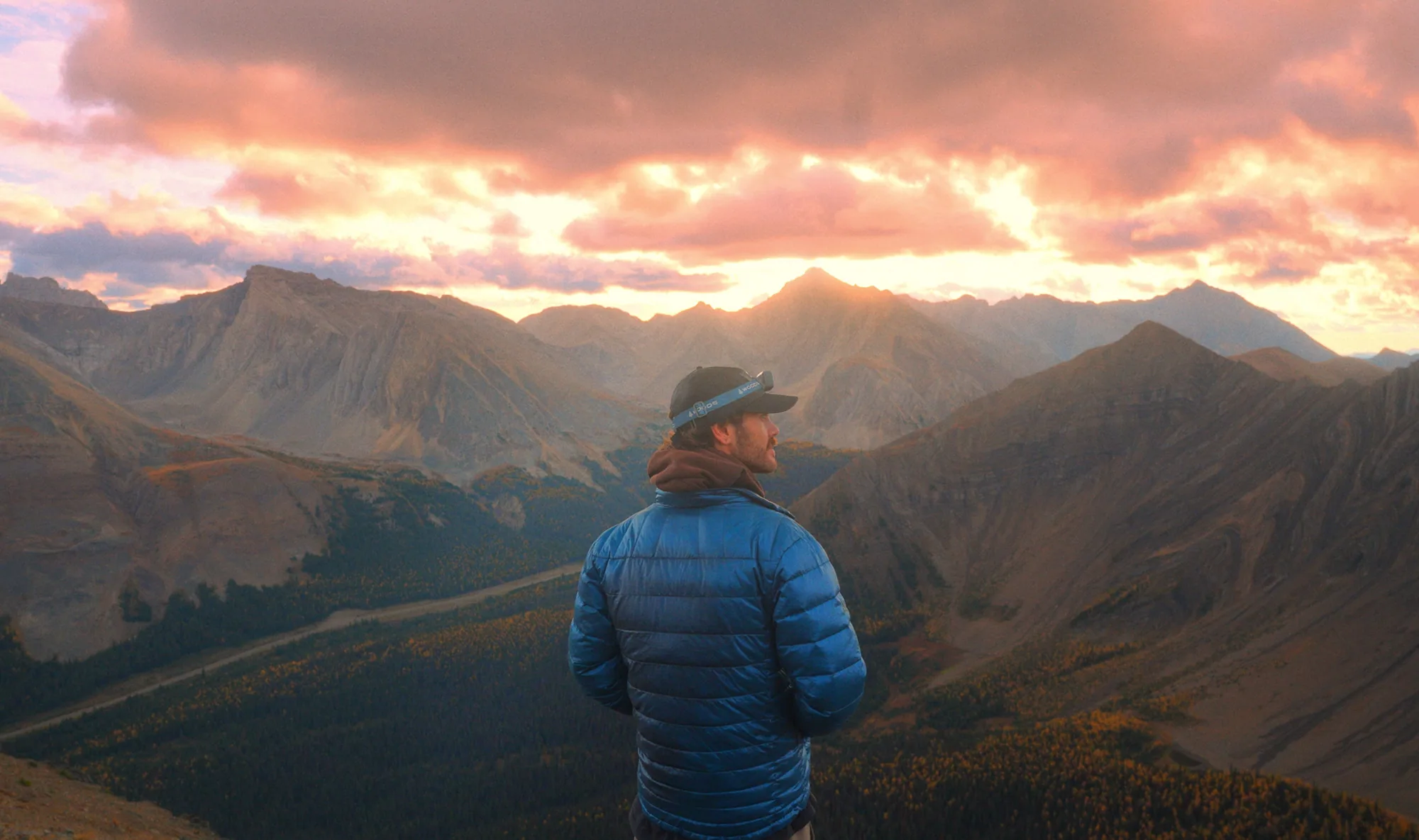 A hiker looking across Pocaterra Ridge while warm light breaks over the mountains.