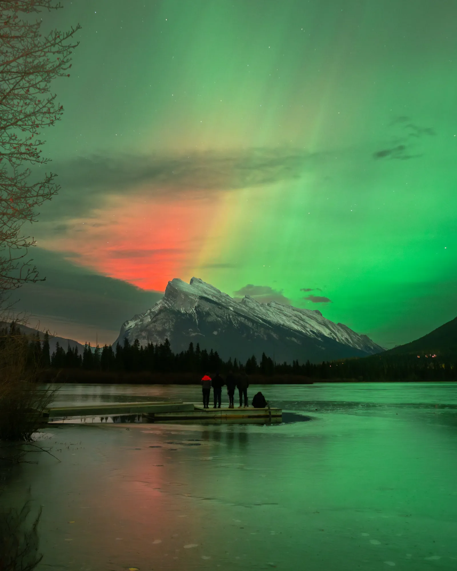 A quiet dock facing Mount Rundle beneath a green aurora.